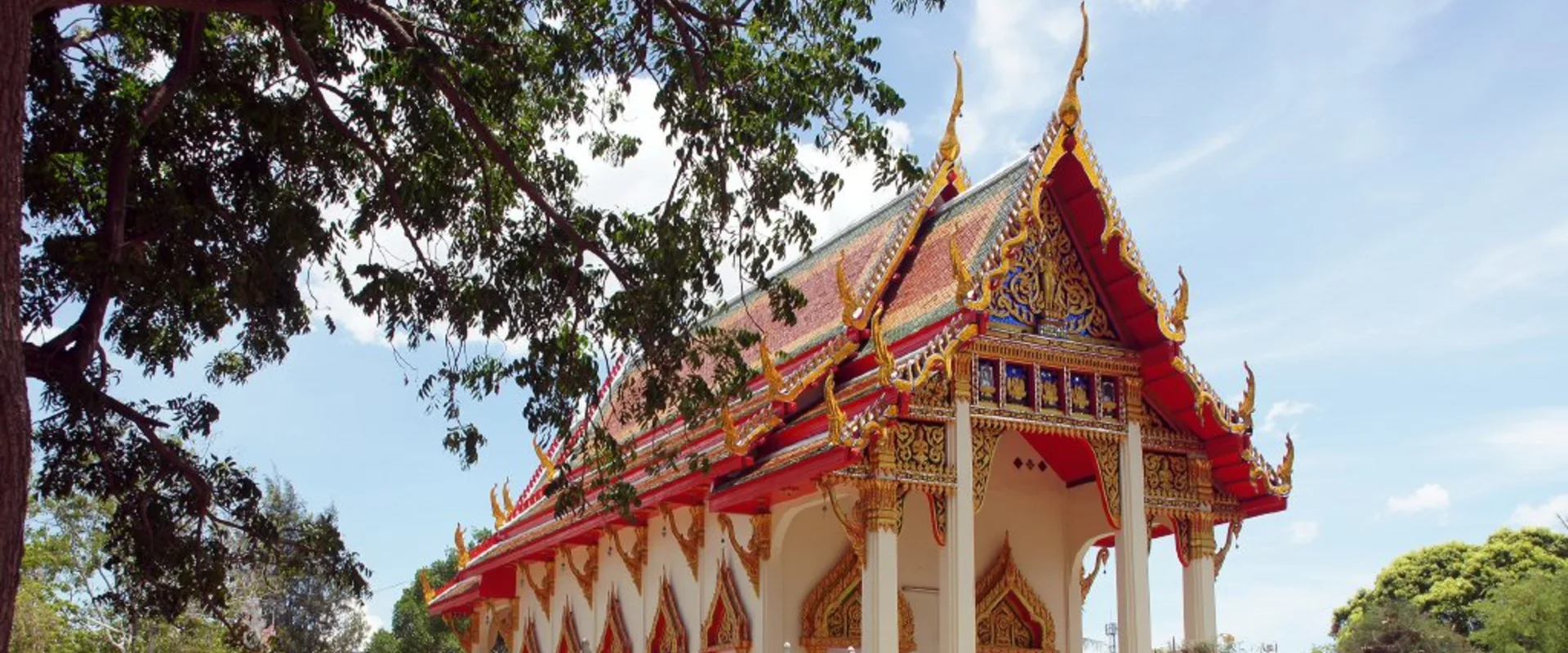 Decorated temple hall at Wat Bo Fai in Hua Hin, with a red tiled roof, gold gable and white boundary wall.