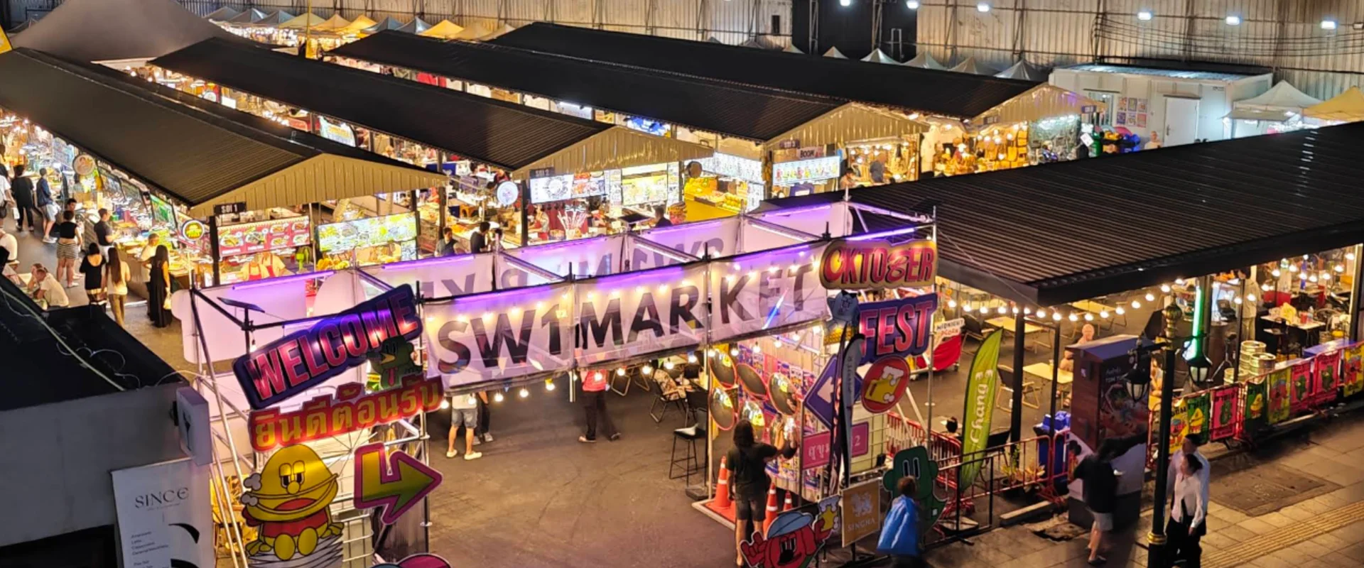 SW1 Market entrance sign and illuminated food stalls near Sukhumvit Soi 12 in Bangkok at night.