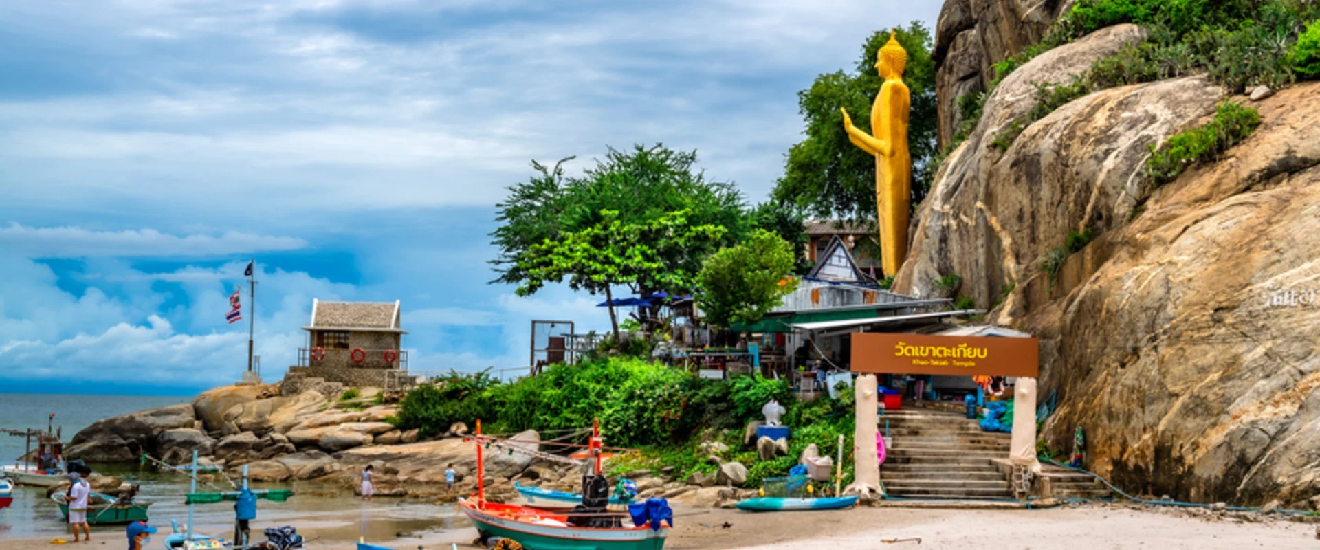 Coastal entrance steps and the named Wat Khao Takiap sign, with a standing golden Buddha beside the rocky hill.