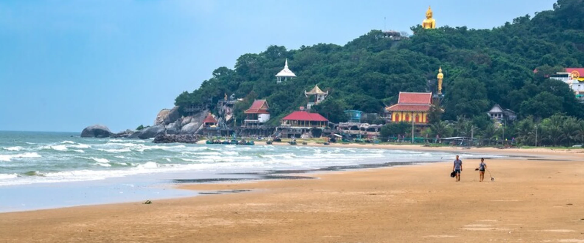 Khao Tao Beach with a sandy shore, waves and the distinctive Wat Tham Khao Tao headland beyond.