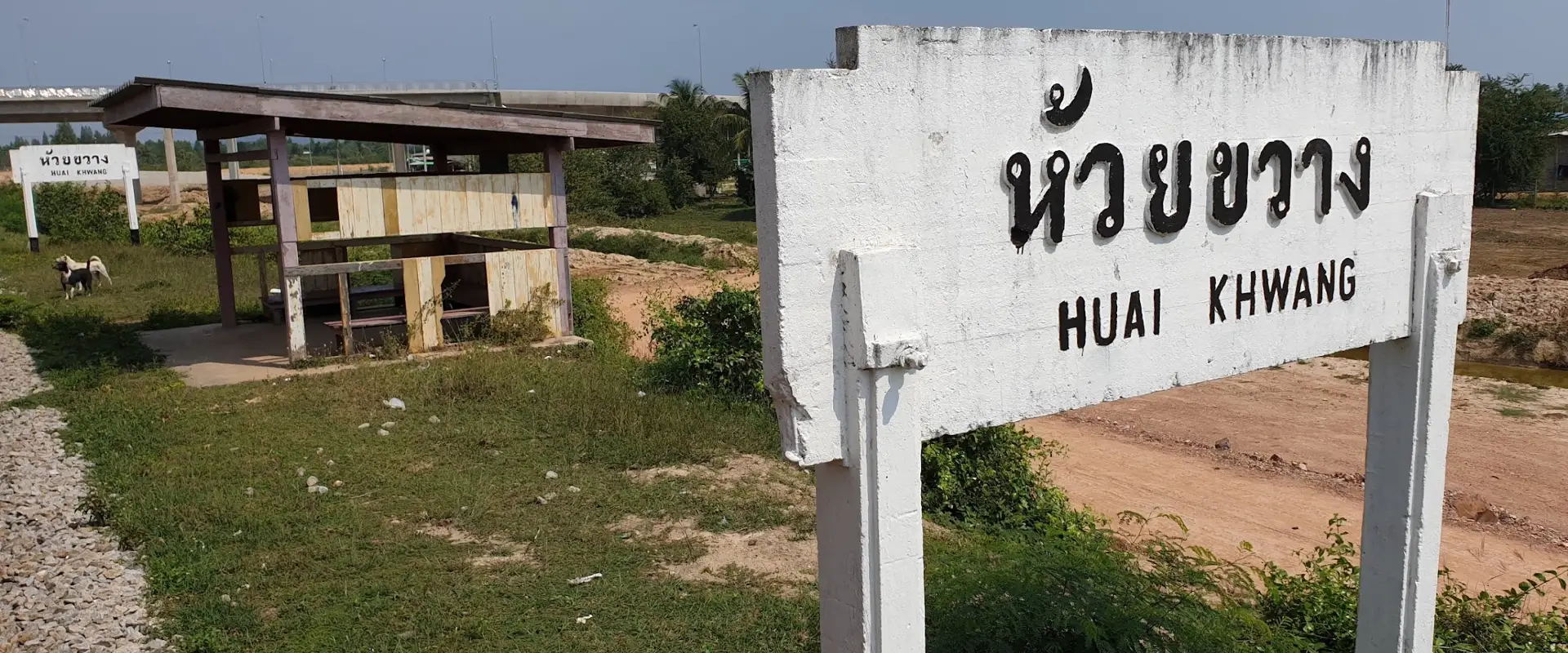 Historical photograph of the bilingual Huai Khwang railway halt sign and old wooden waiting shelter in Sila Loi.