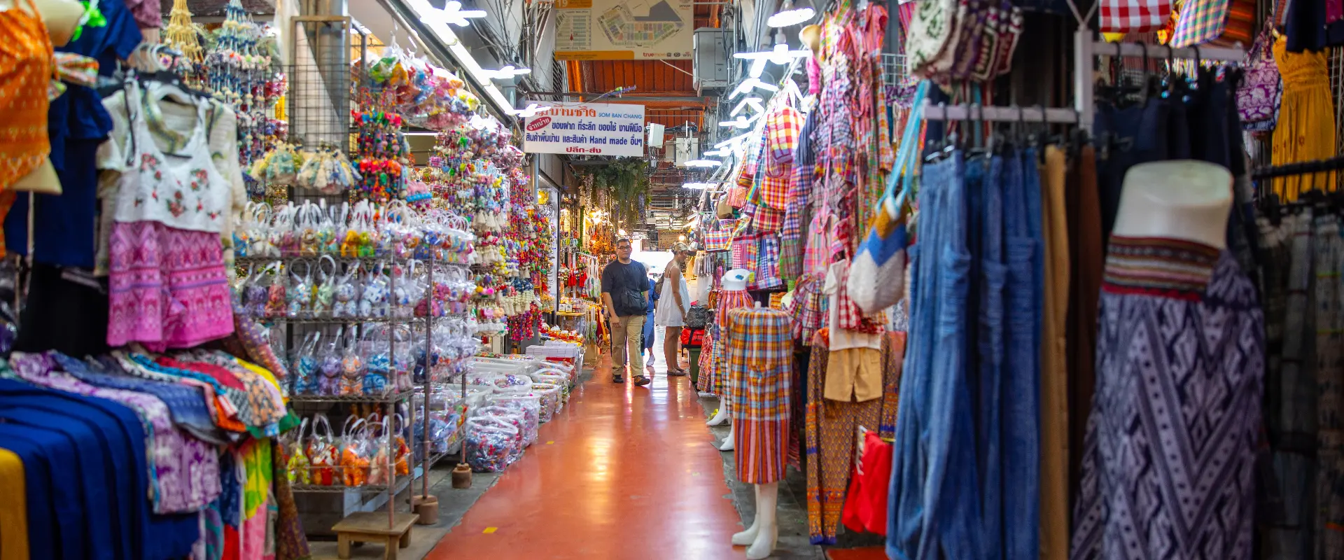 Colourful clothing and souvenir stalls along a covered alley at Chatuchak Weekend Market, Bangkok.