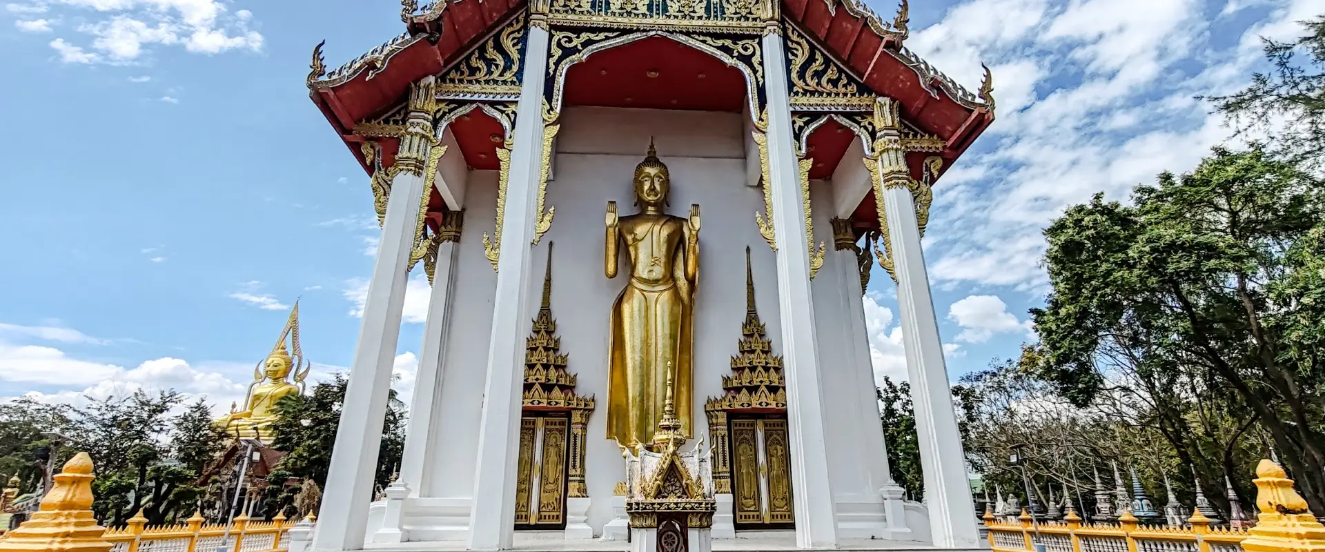 White temple hall with a standing golden Buddha and blue-and-gold gable decoration at Wat Marikathaywan, Cha-am.